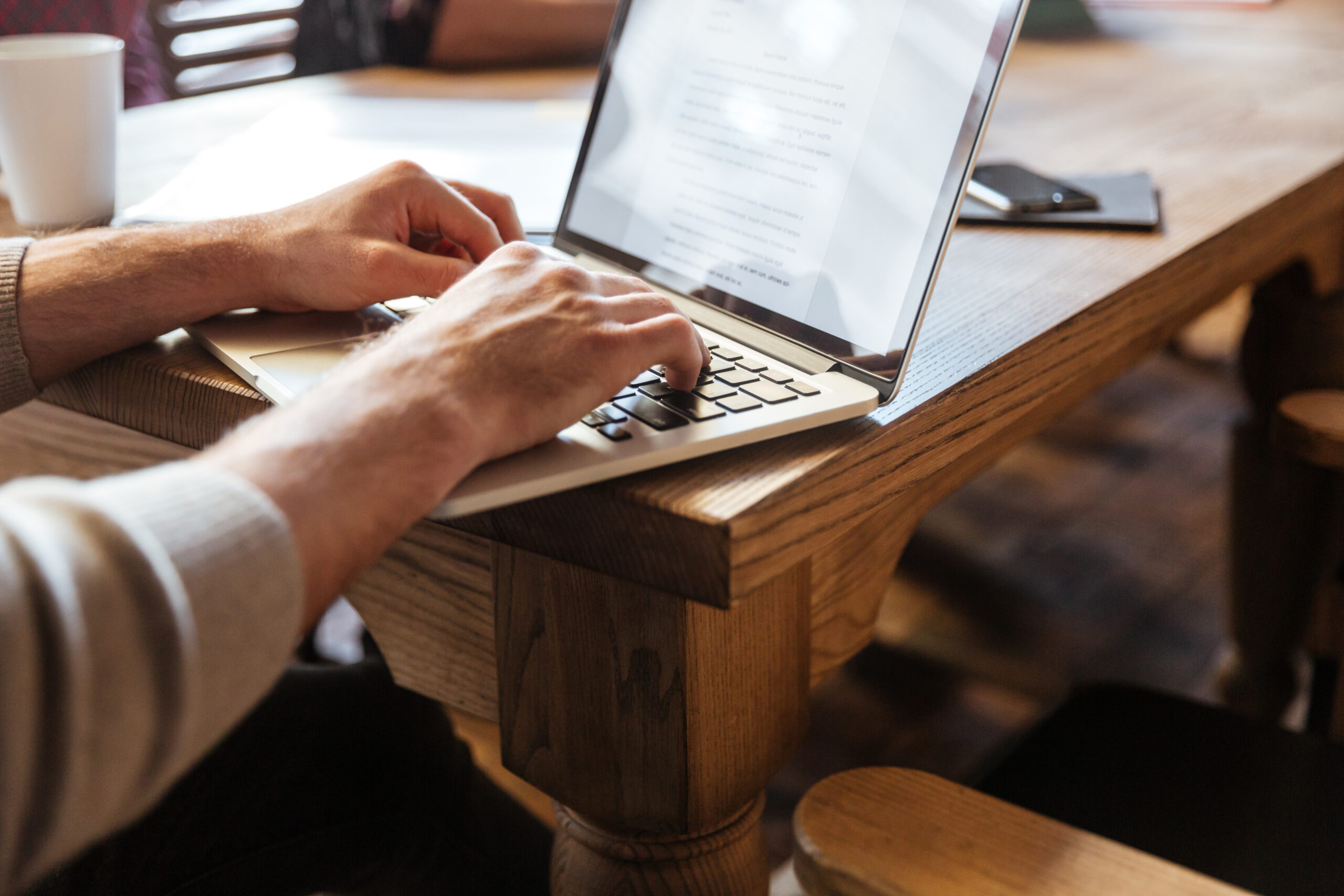 Cropped photo of young concentrated man sitting in office and coworking with laptop.